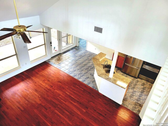 unfurnished living room with dark wood-type flooring, ceiling fan, sink, and high vaulted ceiling