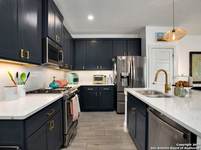 kitchen with light wood-type flooring, backsplash, stainless steel appliances, sink, and hanging light fixtures