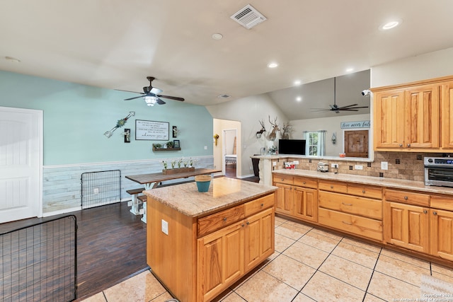 kitchen featuring light wood-type flooring, backsplash, a kitchen island, ceiling fan, and vaulted ceiling