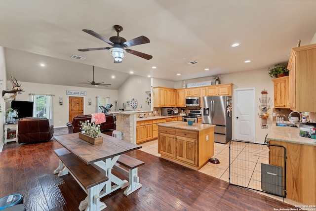 kitchen featuring light wood-type flooring, stainless steel appliances, kitchen peninsula, ceiling fan, and lofted ceiling