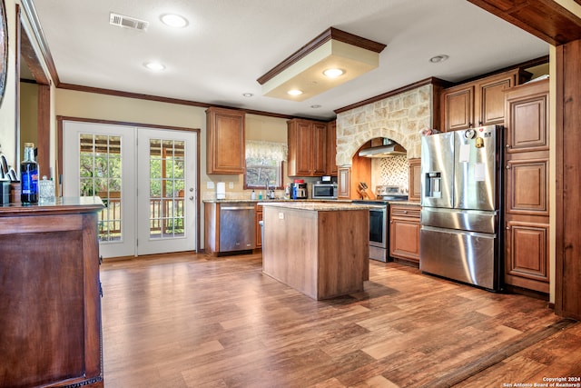 kitchen with ornamental molding, stainless steel appliances, range hood, wood-type flooring, and a kitchen island