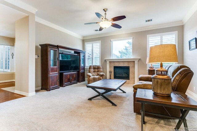 living room featuring ceiling fan, a tile fireplace, wood-type flooring, and ornamental molding