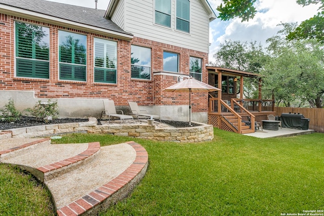 rear view of property with a deck, brick siding, a shingled roof, a yard, and a patio area