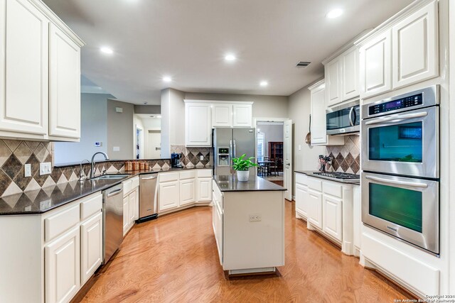 kitchen featuring light wood-type flooring, tasteful backsplash, stainless steel appliances, kitchen peninsula, and sink