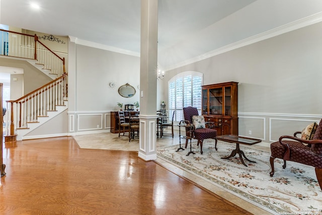 sitting room with a decorative wall, wood finished floors, stairs, ornamental molding, and ornate columns