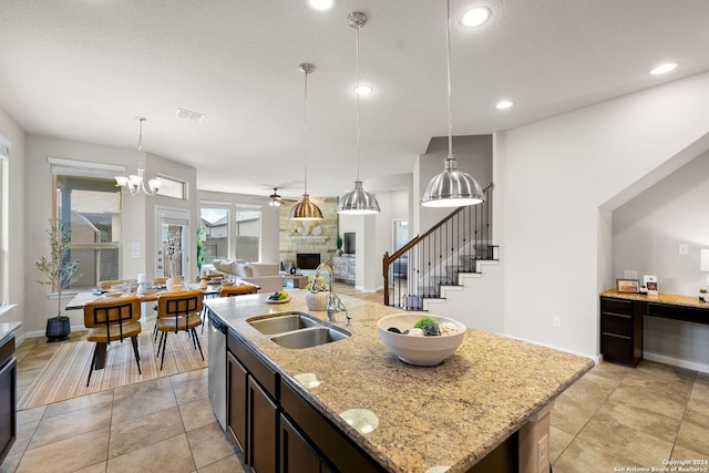 kitchen featuring ceiling fan with notable chandelier, stainless steel dishwasher, visible vents, a stone fireplace, and a sink