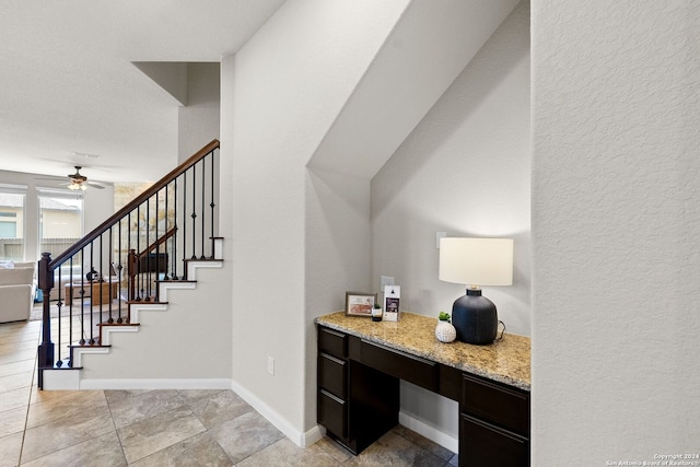 interior space with a textured wall, built in study area, baseboards, and ceiling fan