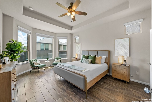 bedroom with a ceiling fan, a tray ceiling, baseboards, and wood finish floors