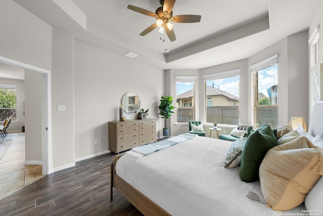 bedroom featuring multiple windows, a tray ceiling, baseboards, and wood finished floors