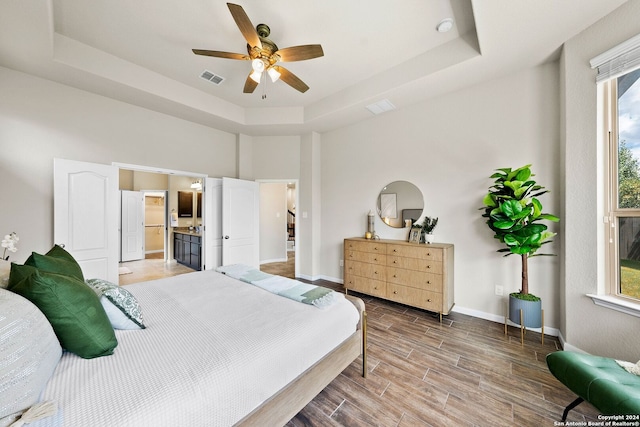 bedroom with a tray ceiling, visible vents, baseboards, and wood finish floors