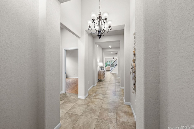 corridor with a notable chandelier, baseboards, a towering ceiling, light tile patterned floors, and stairs