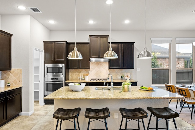 kitchen with stainless steel appliances, under cabinet range hood, a breakfast bar, and light stone counters