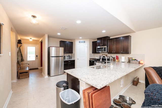 kitchen with appliances with stainless steel finishes, a sink, light stone countertops, a peninsula, and a kitchen bar