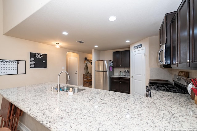 kitchen featuring arched walkways, light stone counters, a peninsula, stainless steel appliances, and a sink