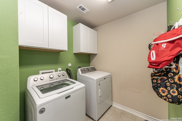 laundry room featuring light tile patterned floors, a textured ceiling, cabinets, and washer and dryer