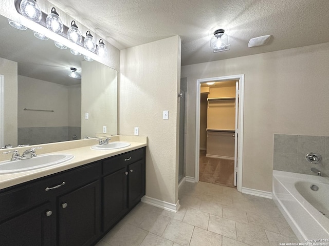 bathroom with a garden tub, a spacious closet, a textured ceiling, and a sink