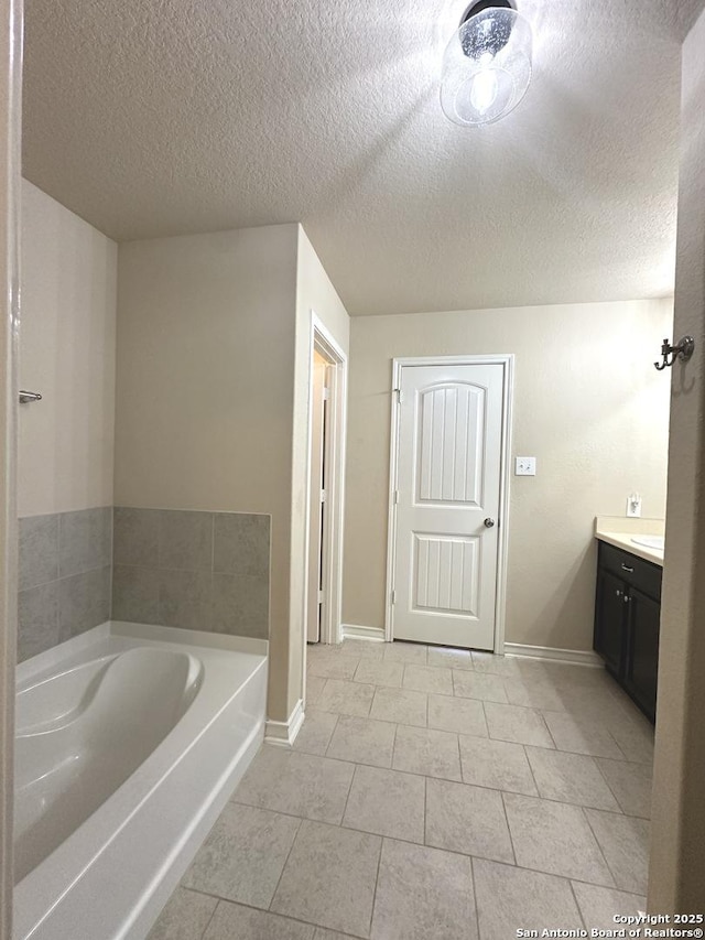 full bathroom with a textured ceiling, vanity, baseboards, a bath, and tile patterned floors