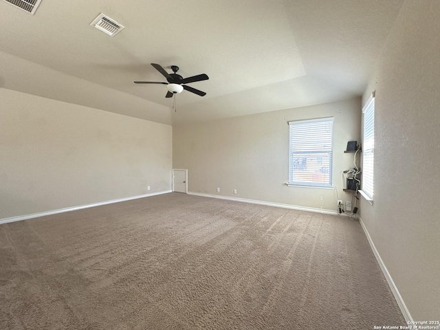 carpeted spare room with a ceiling fan, baseboards, visible vents, and a tray ceiling