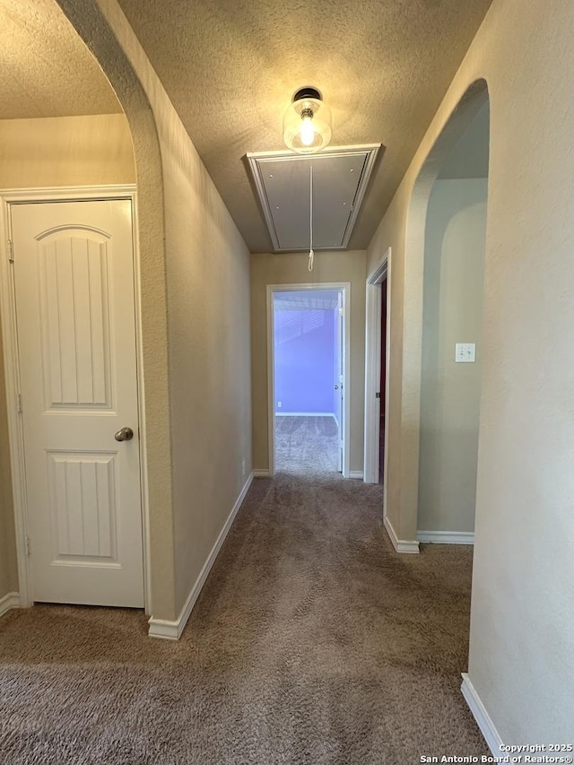 hall featuring carpet floors, attic access, arched walkways, and a textured ceiling