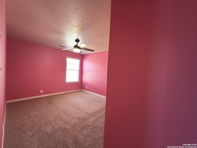 carpeted spare room featuring a ceiling fan, visible vents, a textured ceiling, and baseboards