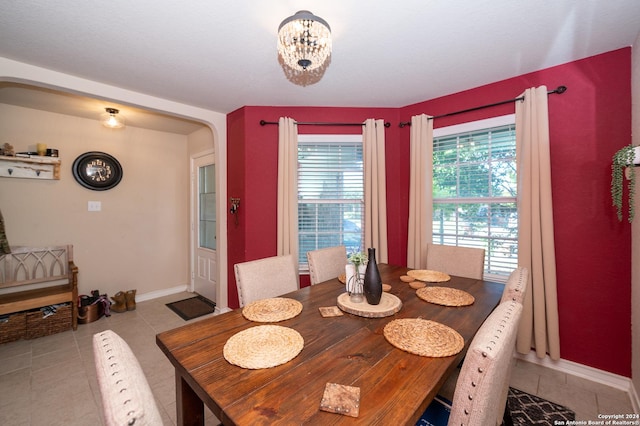 dining area featuring light tile patterned floors, baseboards, arched walkways, and a chandelier