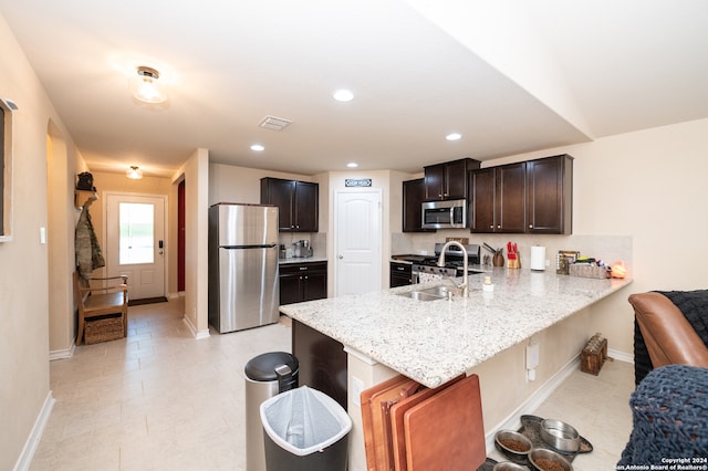 kitchen with kitchen peninsula, light stone counters, sink, and appliances with stainless steel finishes