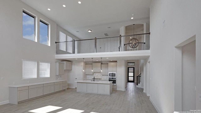 kitchen featuring pendant lighting, stainless steel microwave, an island with sink, sink, and a notable chandelier