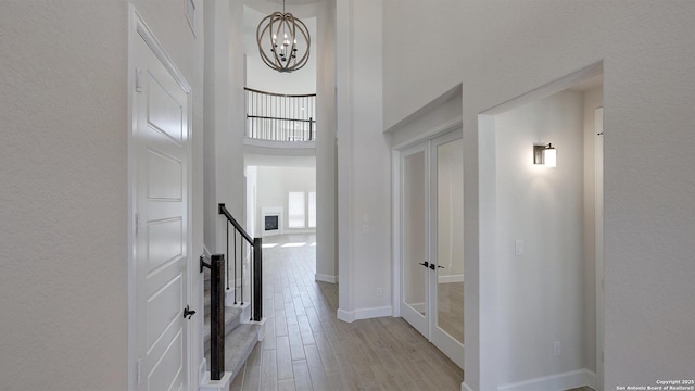 hallway featuring a towering ceiling, light hardwood / wood-style flooring, and a chandelier