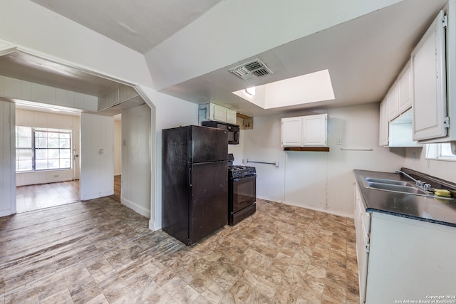 kitchen with black appliances, white cabinetry, a skylight, and sink