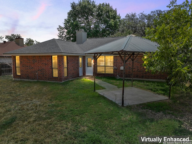 back house at dusk featuring a lawn and a patio area