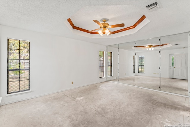 empty room featuring a textured ceiling, a tray ceiling, plenty of natural light, and ceiling fan