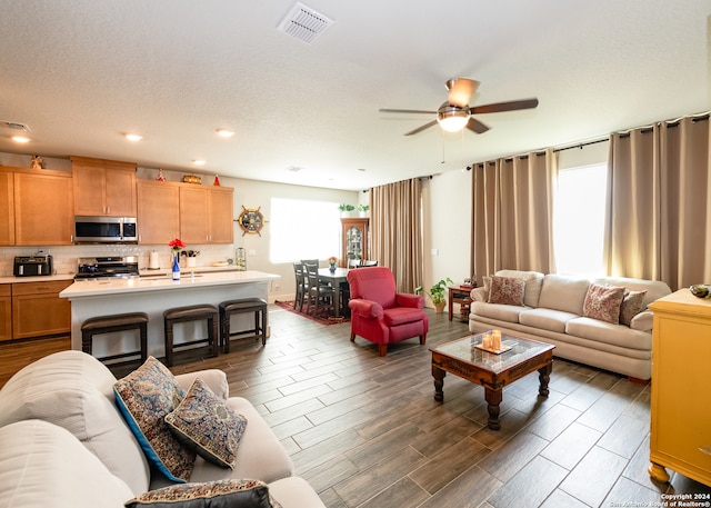 living room featuring dark hardwood / wood-style flooring, ceiling fan, and a textured ceiling