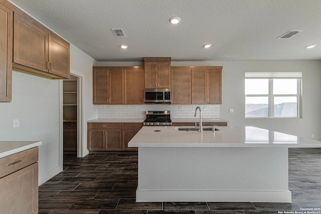 kitchen featuring appliances with stainless steel finishes, a sink, light countertops, wood finish floors, and backsplash