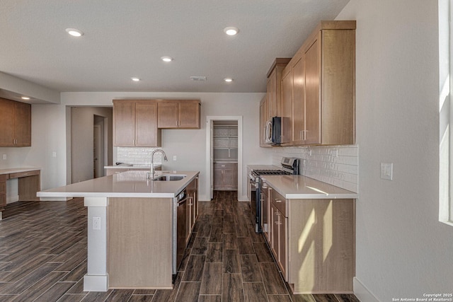 kitchen featuring a kitchen island with sink, stainless steel appliances, a sink, light countertops, and wood tiled floor