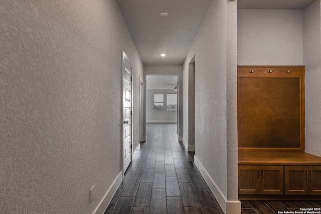 hallway featuring a textured wall, wood finish floors, and baseboards