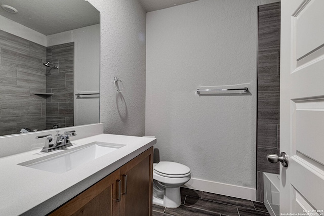 full bathroom featuring toilet, a textured wall, wood finish floors, and vanity