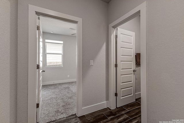 corridor with a textured wall, wood finish floors, and baseboards