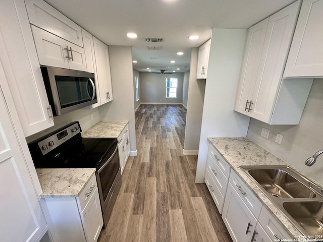 kitchen featuring white cabinets, wood finished floors, appliances with stainless steel finishes, and a sink