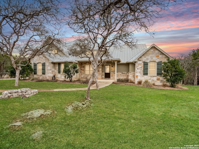 view of front of home with stone siding, a yard, a standing seam roof, and metal roof