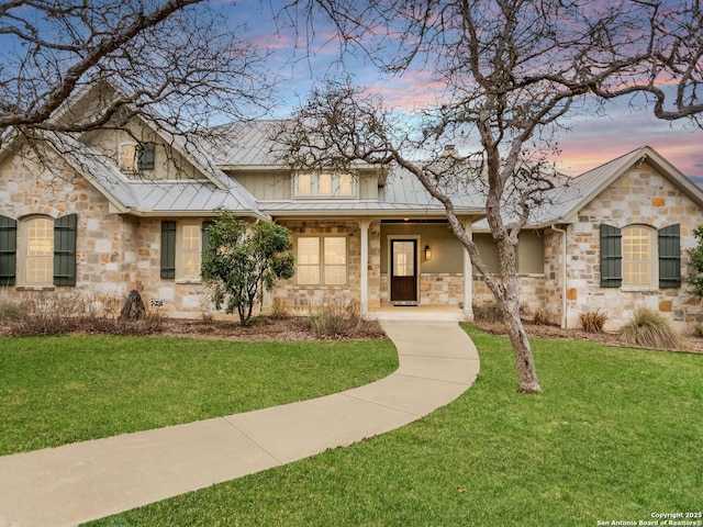 view of front of home with a lawn, stone siding, metal roof, a standing seam roof, and a porch