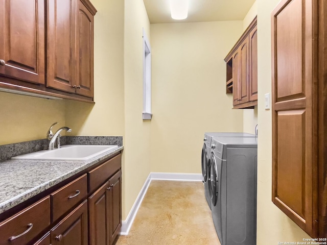 clothes washing area featuring baseboards, a sink, cabinet space, and washer and dryer