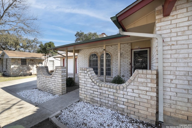 property entrance featuring covered porch, concrete driveway, and brick siding