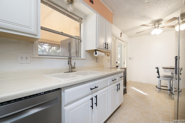 kitchen with light countertops, backsplash, stainless steel dishwasher, white cabinetry, and a sink