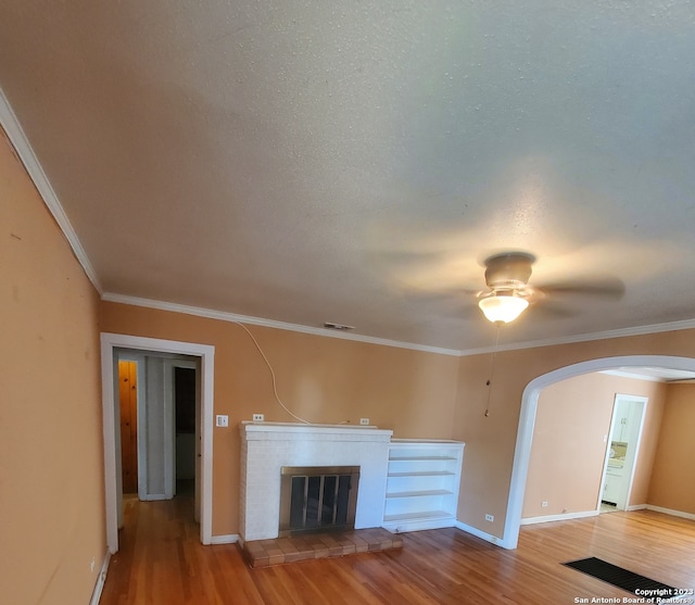 unfurnished living room with a fireplace, ornamental molding, wood-type flooring, and ceiling fan