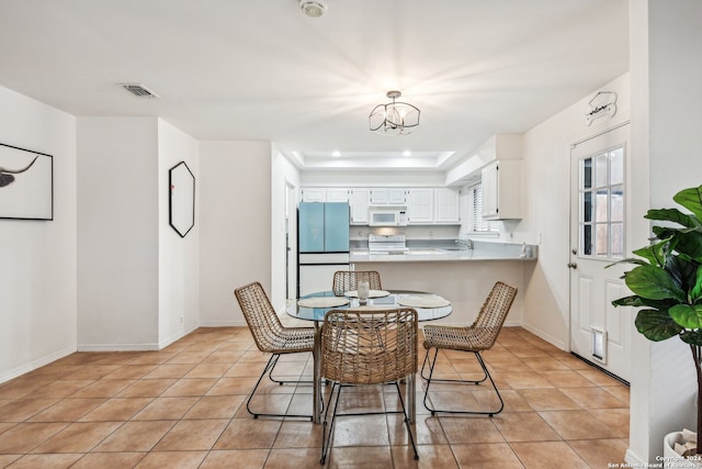 tiled dining area with a tray ceiling and a chandelier