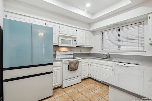 kitchen with a raised ceiling, white appliances, light tile patterned floors, sink, and white cabinetry