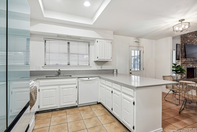 kitchen with white dishwasher, kitchen peninsula, sink, a brick fireplace, and white cabinetry