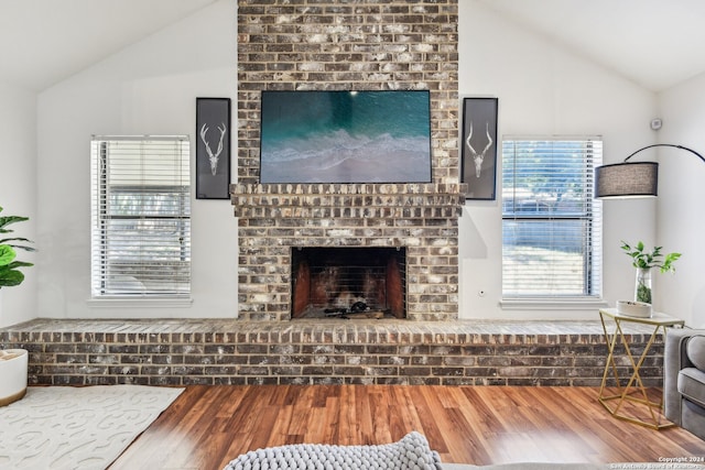 living room with vaulted ceiling, hardwood / wood-style floors, and a brick fireplace