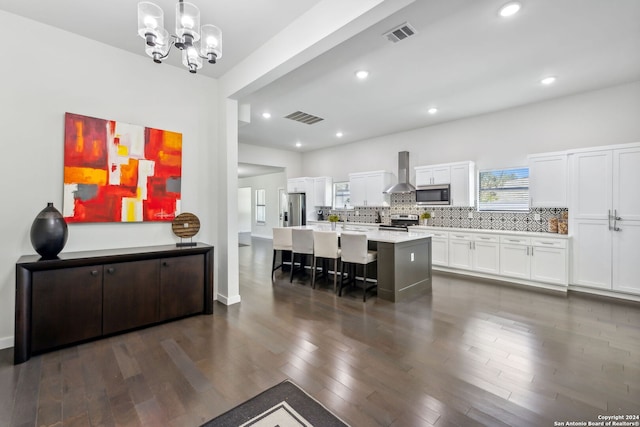 kitchen featuring wall chimney exhaust hood, a kitchen bar, white cabinetry, hanging light fixtures, and stainless steel appliances