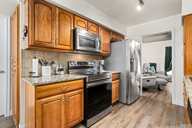 kitchen with appliances with stainless steel finishes, light stone counters, backsplash, and light hardwood / wood-style floors